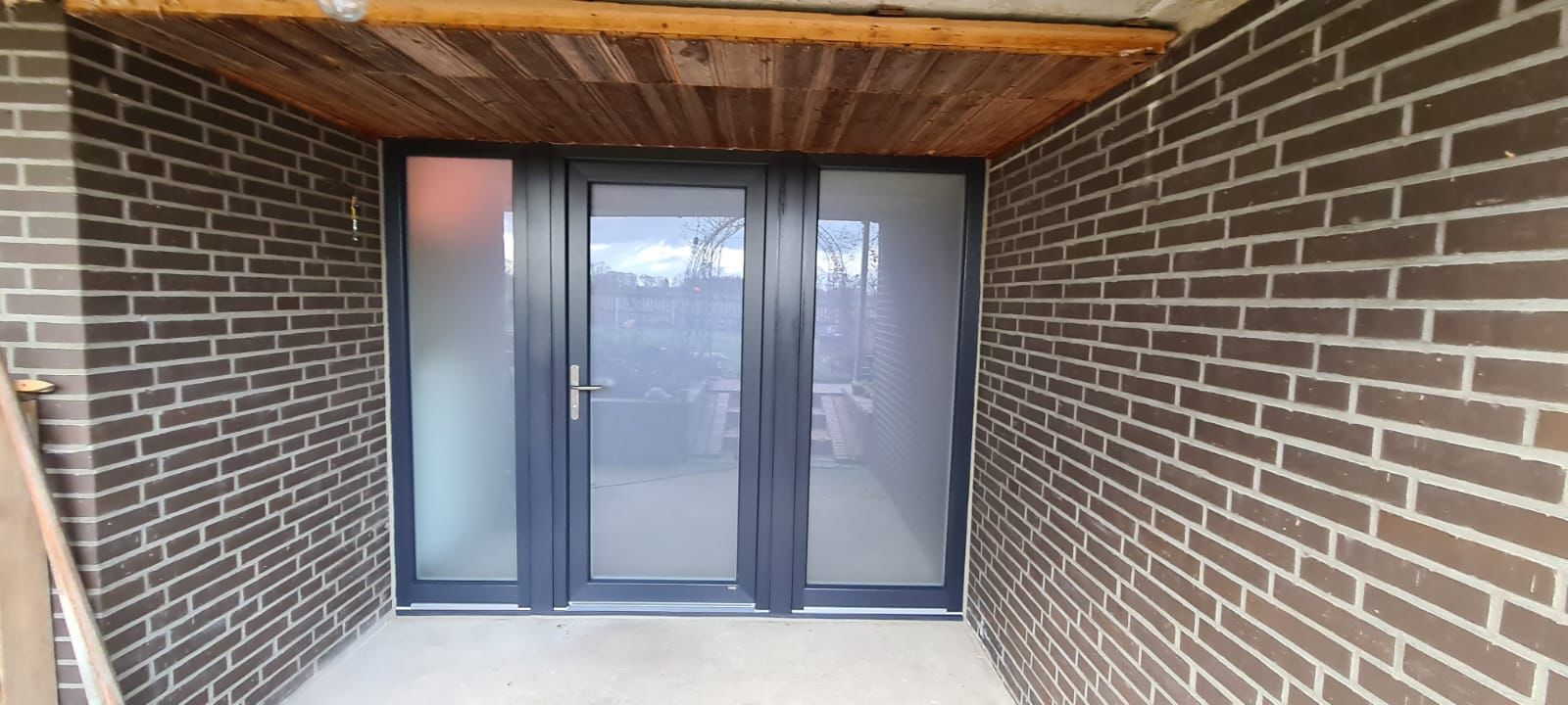 Eine Ziegelwand mit einer Glastür und einer Holzdecke.