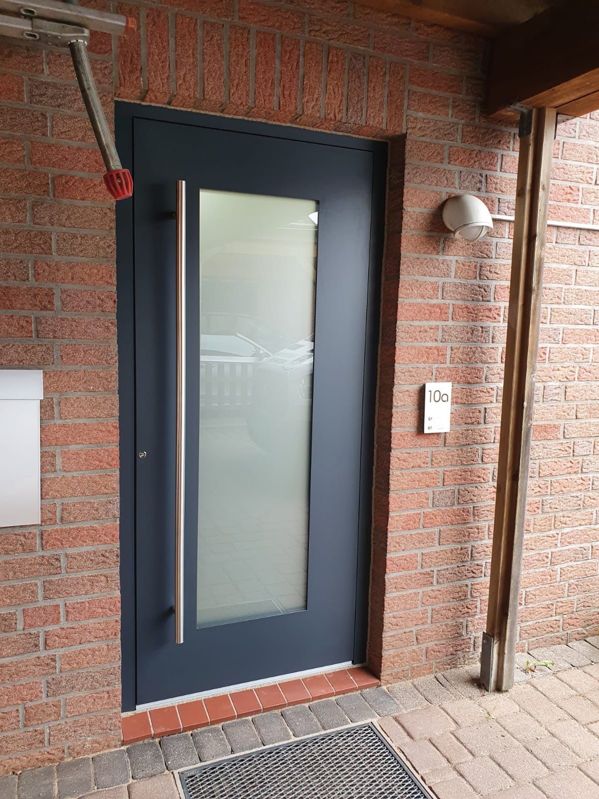 An einer Backsteinmauer befindet sich eine schwarze Tür mit einem Glasfenster.