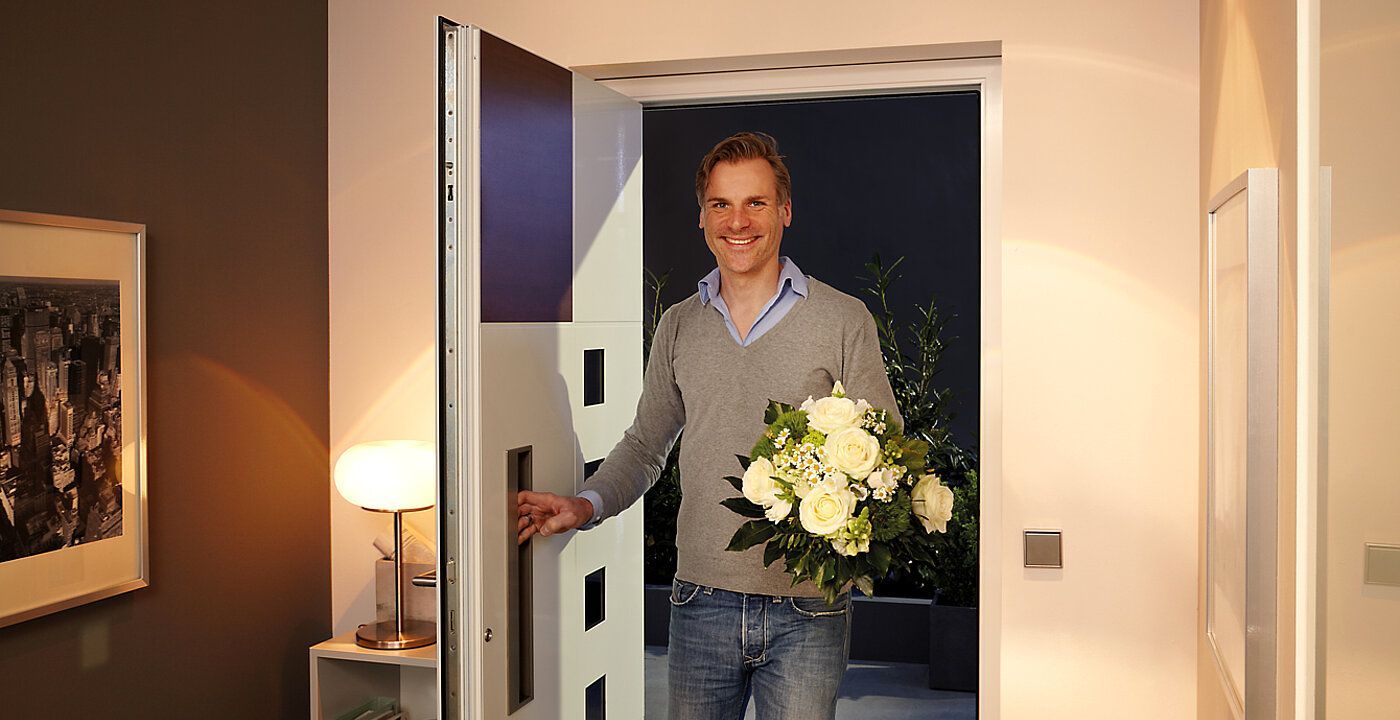 Ein Mann hält einen Blumenstrauß in der Hand und steht vor einer Tür.