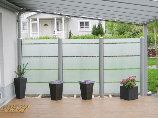 Eine Terrasse mit Zaun und Topfpflanzen vor einem Haus.