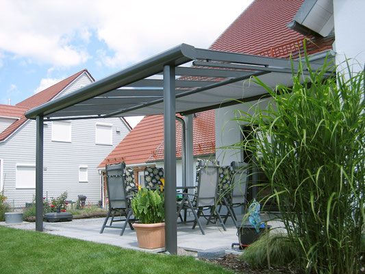 Eine Terrasse mit Pergola und Stühlen vor einem Haus.
