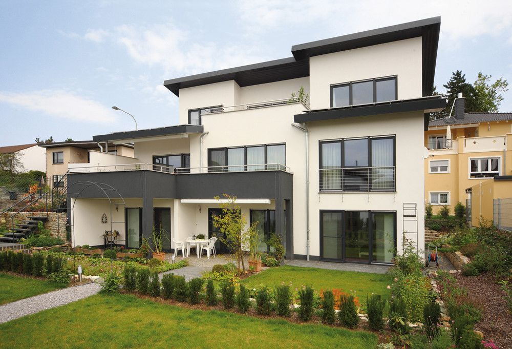 Ein großes weißes Haus mit vielen Fenstern und einer großen Wiese davor.