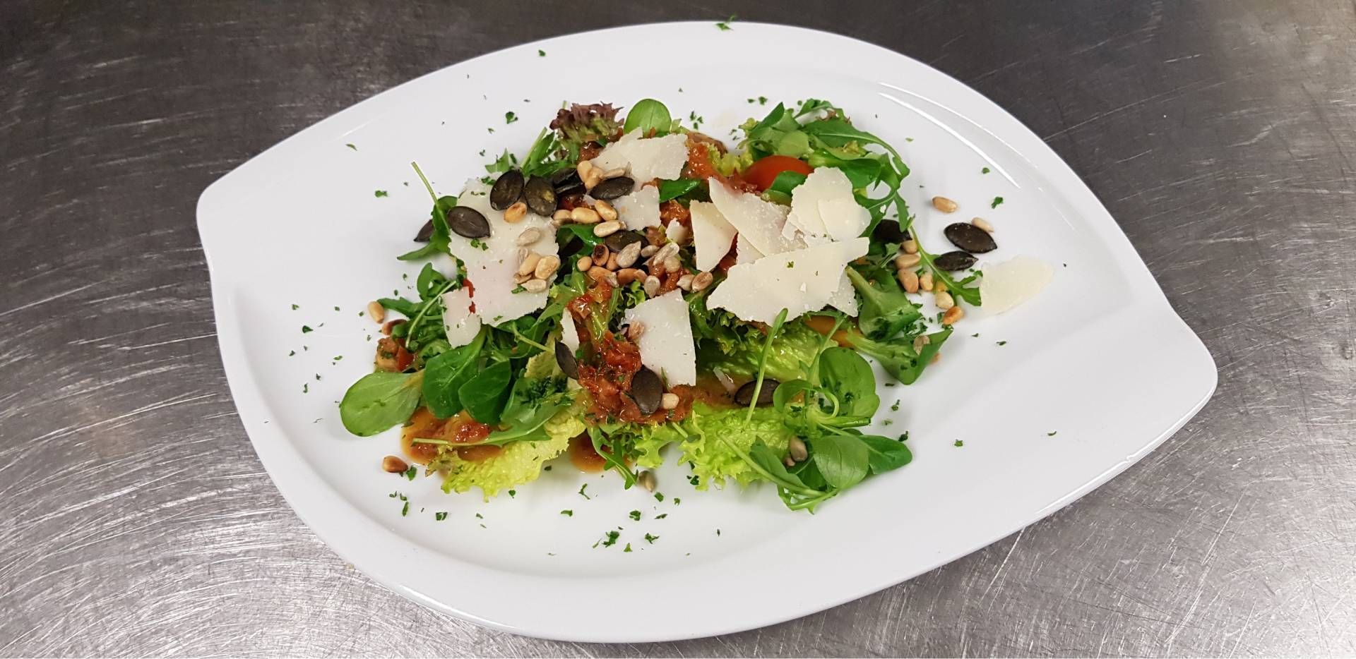 Gourmetsalat mit Blattgemüse, Kräutern und gehobeltem Käse auf einem weissen Teller