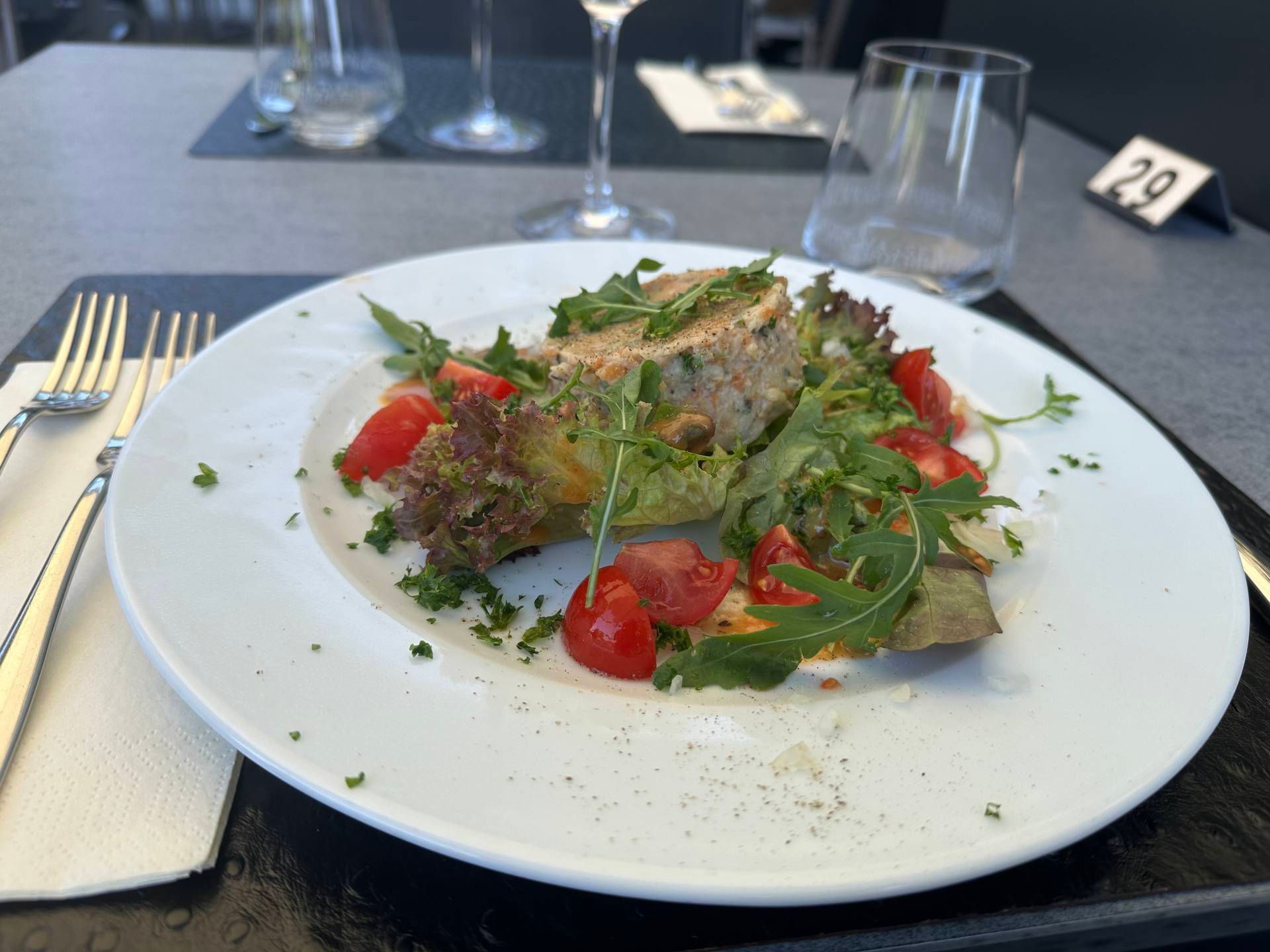 Gourmetsalat mit Blattgemüse und Kirschtomaten auf einem weissen Teller an einem Restauranttisch