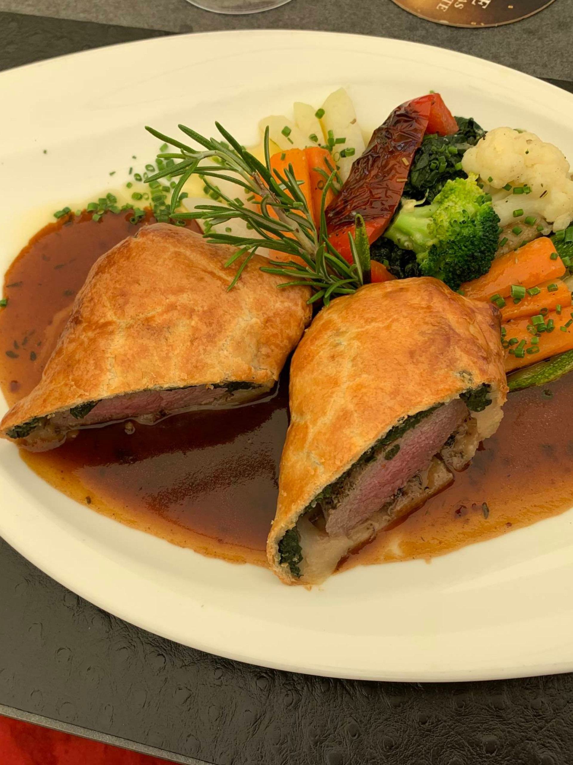 Gourmetgericht mit zwei gebratenen, gefüllten Stücken, brauner Sosse und Gemüse auf einem weissen, ovalen Teller.
