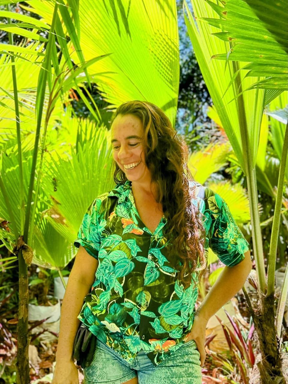 Mujer cuidando plántulas en un invernadero con bancos de madera. Hileras de plantas jóvenes.
