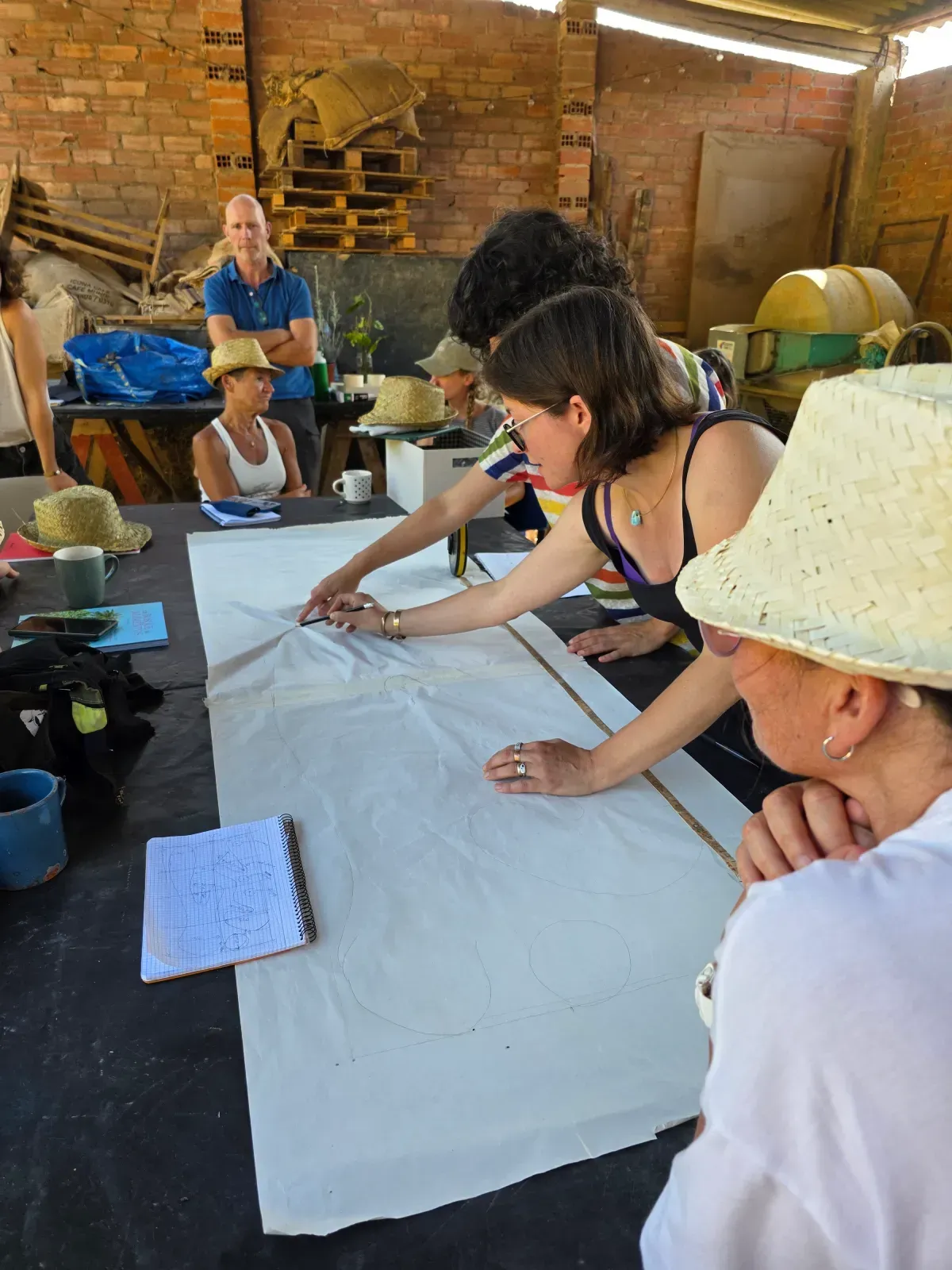 Personas trabajando juntas, dibujando en un papel blanco grande sobre una mesa en un taller.