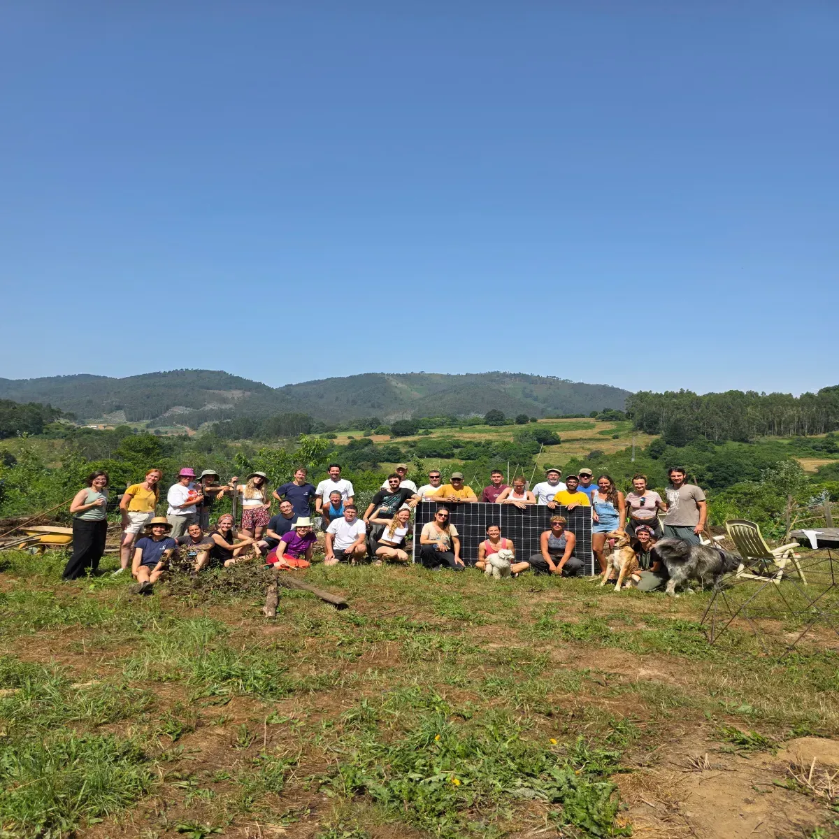 Grupo de personas sonriendo, posando al aire libre. Paneles solares detrás, campo, cielo azul y colinas verdes.