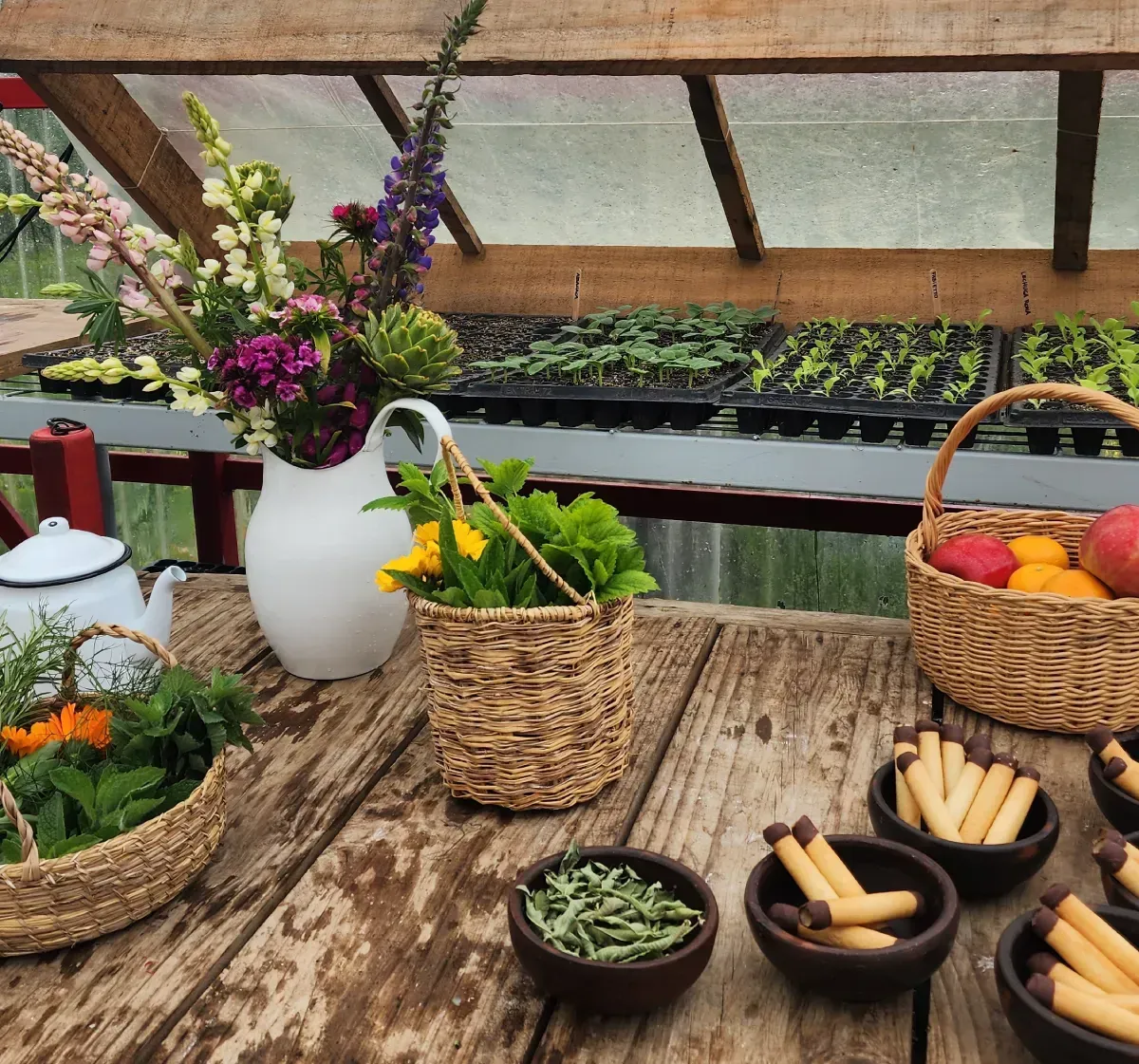 Mesa rústica con flores, productos y pequeñas cestas, fondo de invernadero.