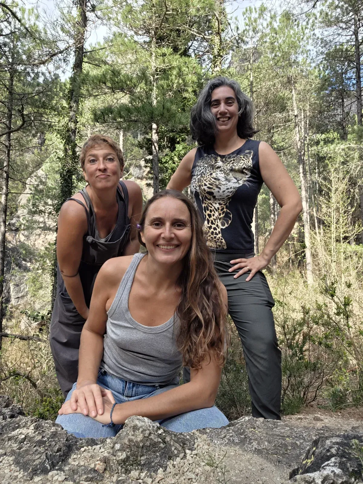 Tres mujeres posando en un bosque; una arrodillada, las demás de pie, todas sonriendo.