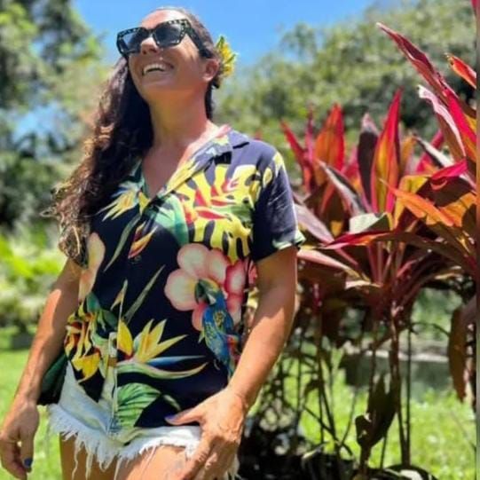 Mujer cuidando plántulas en un invernadero con bancos de madera. Hileras de plantas jóvenes.