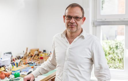 Ein Mann in einem weißen Hemd und mit Brille steht vor einem Tisch.