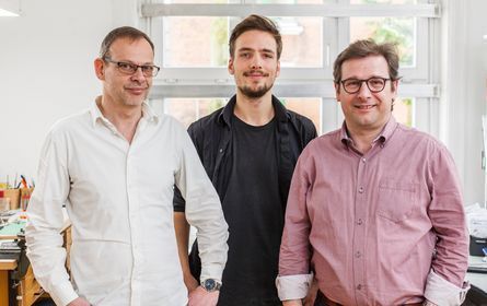 Drei Männer posieren zusammen für ein Foto in einem Büro.