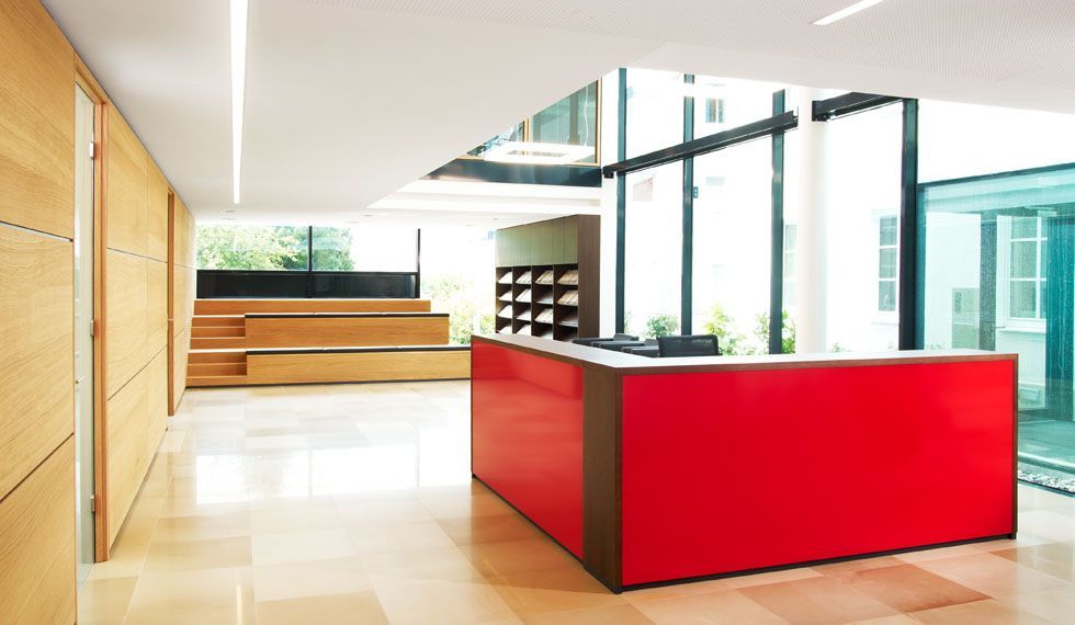 Ein roter Rezeptionstresen in einem Flur mit vielen Fenstern