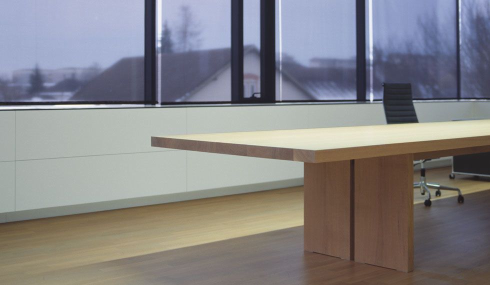 Ein langer Holztisch steht vor einem Fenster