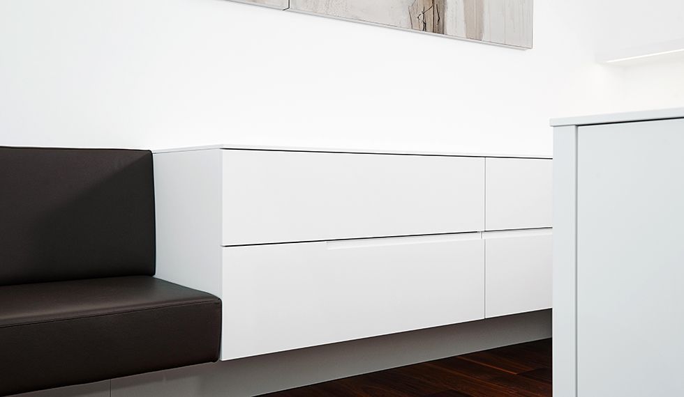 In einem Wartezimmer steht ein Sofa neben einem weißen Schrank.