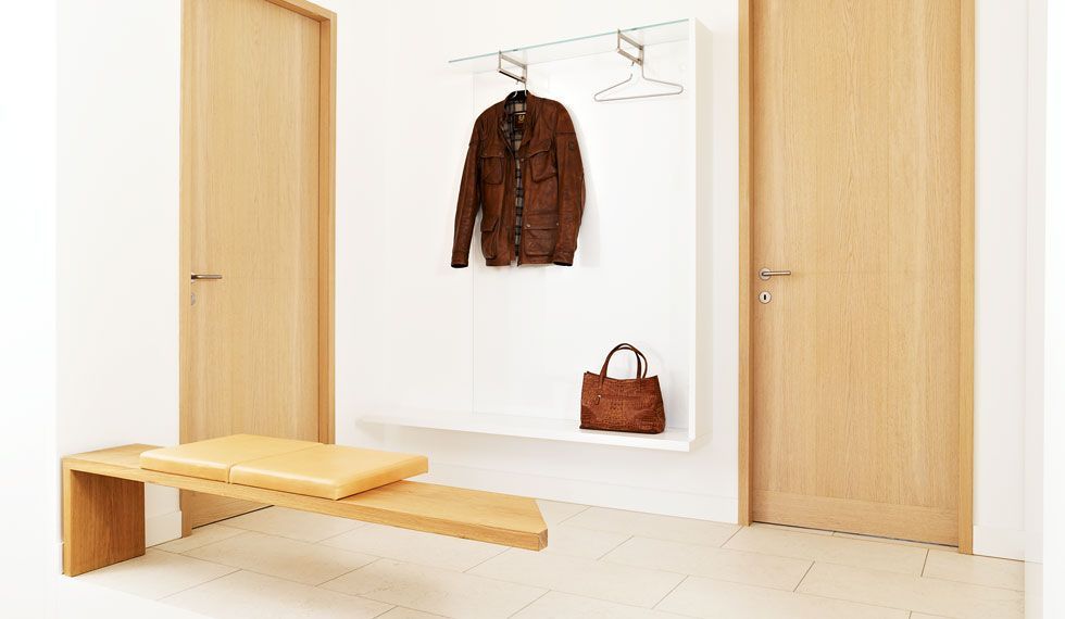 Ein Flur mit einer Bank, einer Garderobe, einer Handtasche und einer Jacke, die an der Wand hängen.