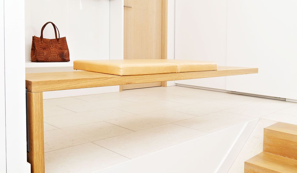 Eine Handtasche liegt auf einem Regal neben einer Holzbank in einem Flur.