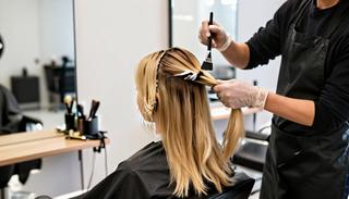 Estilista aplicando mechas rubias en una silla de peluquería, con brocha y guantes.