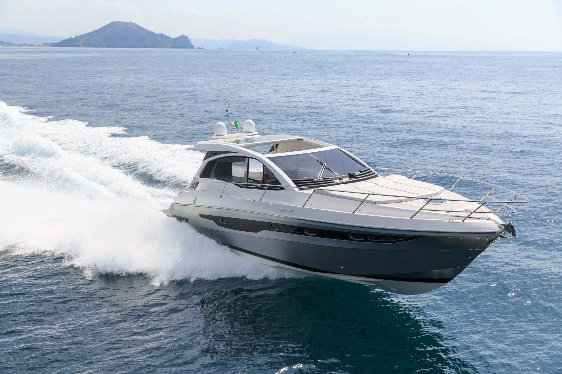 Eine weisse Motoryacht rast über den blauen Ozean, Gischt spritzt, eine Insel ist in der Ferne zu sehen.