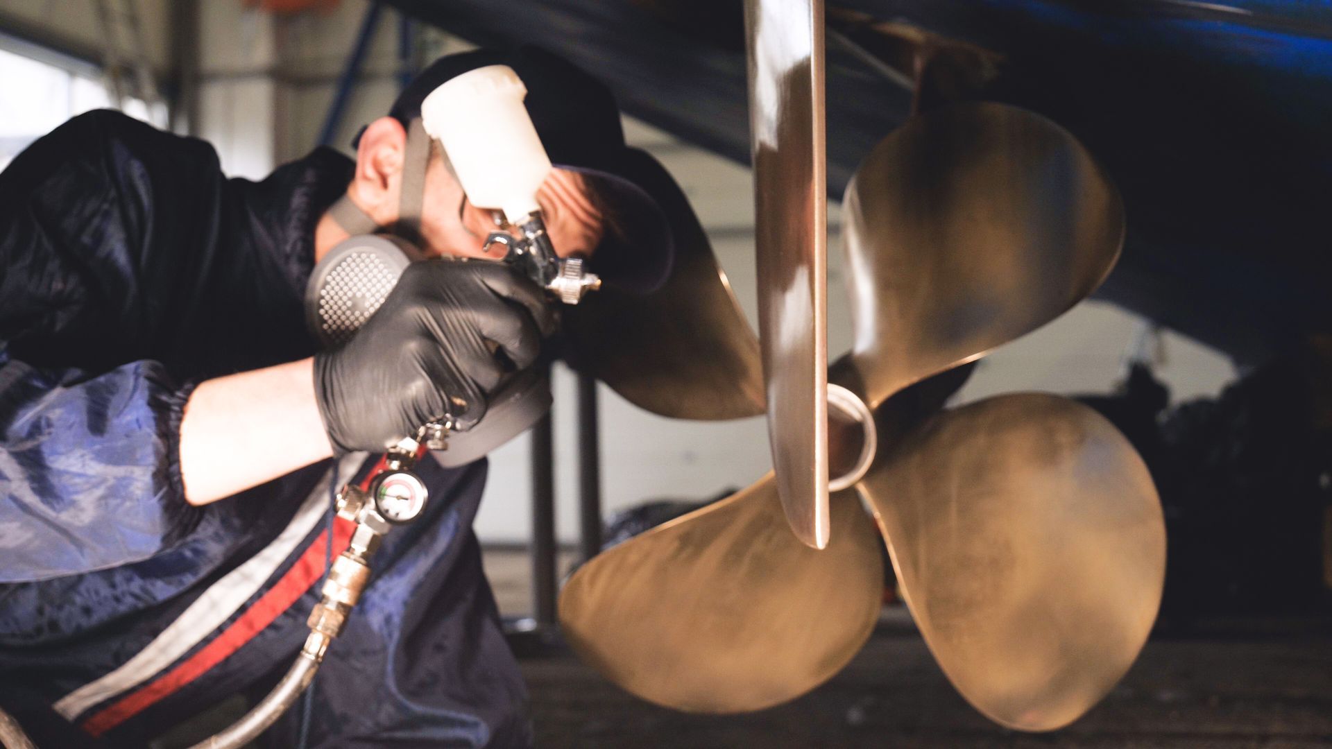 Ein Arbeiter mit Handschuhen und Maske inspiziert eine Schiffsschraube in einer Werkstatt