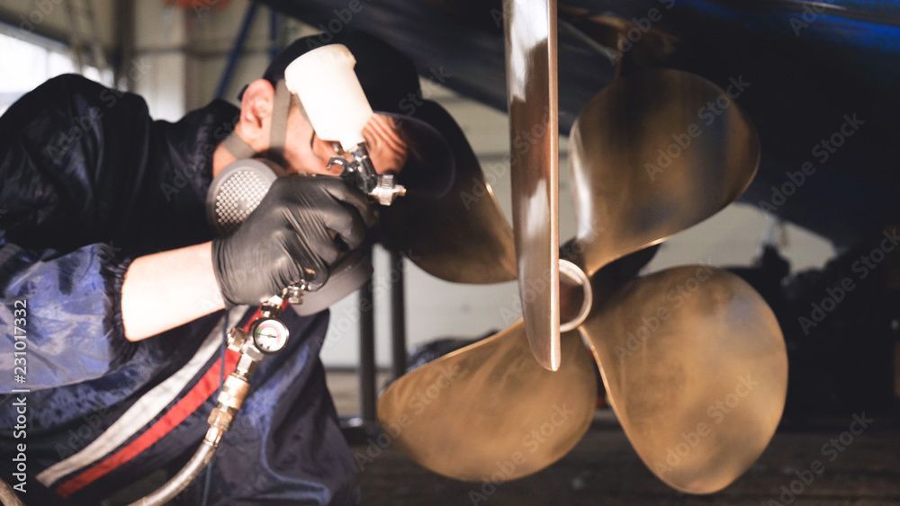 Ein Arbeiter mit Handschuhen und Maske inspiziert eine Schiffsschraube in einer Werkstatt