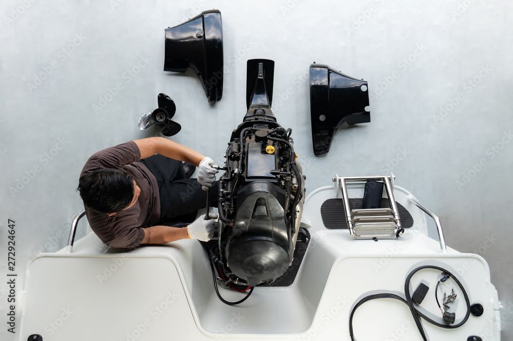 Ein Techniker untersucht ein schwarzes mechanisches Gerät auf einem Tisch, in dessen Nähe lose Teile und Werkzeuge liegen.