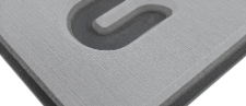 Nahaufnahme einer grauen, strukturierten Metallecke mit einem erhabenen, dunkelgrauen Symbol oder Griffdetail