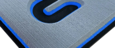 Nahaufnahme eines blau umrandeten, schwarz-grauen, strukturierten Logos auf einer metallischen Oberfläche