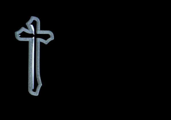 Una cruz de plata flota en el aire sobre un fondo negro.