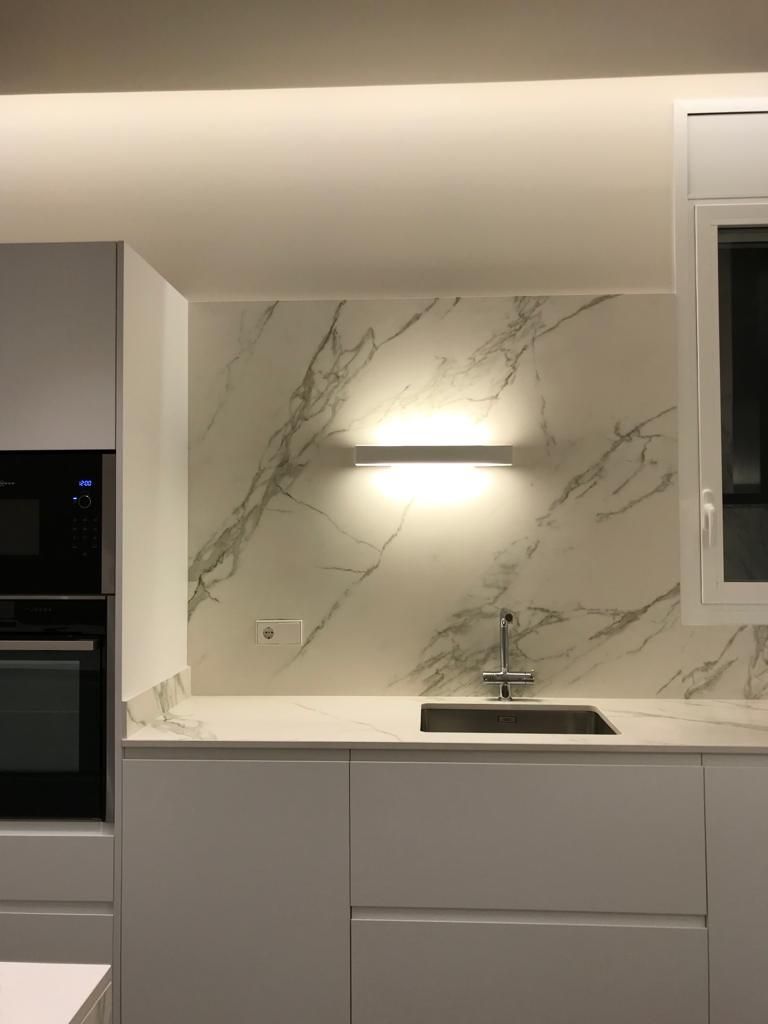 Una cocina con muebles blancos, un fregadero y una pared de mármol.