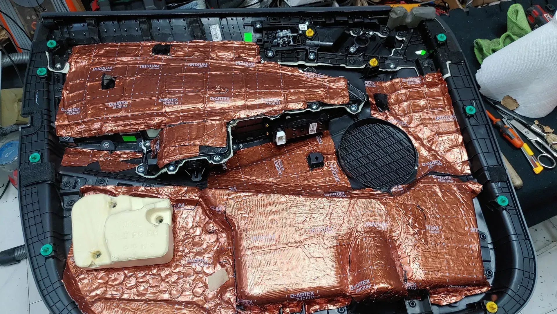 Panel de puerta de automóvil con material insonorizante marrón aplicado, clips verdes y altavoz.