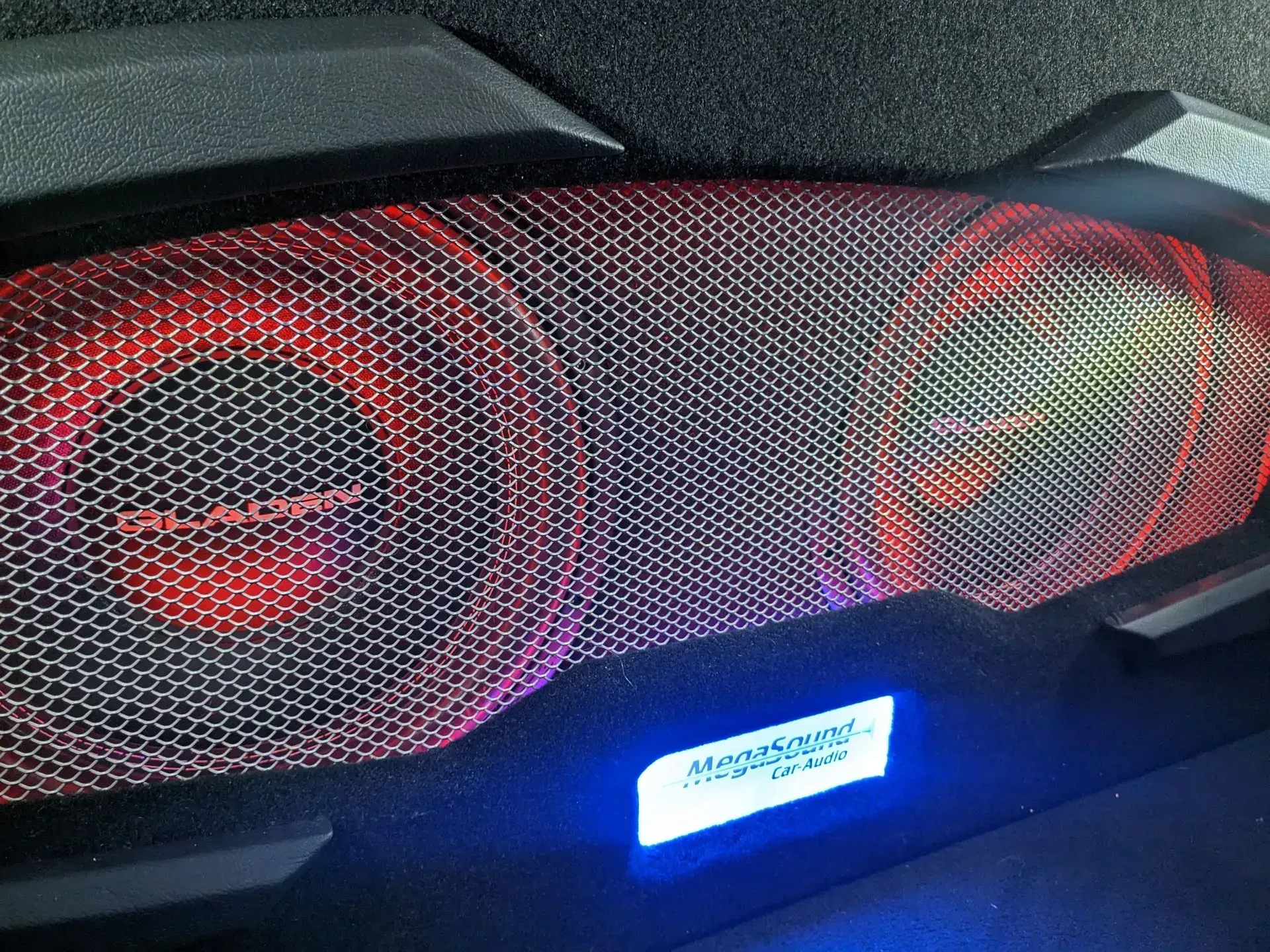 Primer plano de un altavoz con rejilla de malla iluminada con luces rojas. Una luz azul muestra la marca.