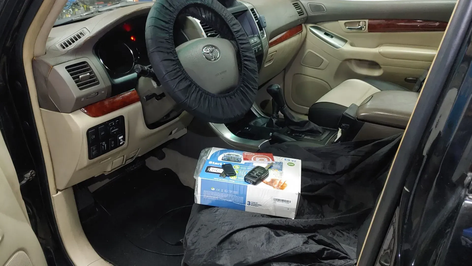 Interior del coche con funda de volante, caja en el suelo y alfombrilla de goma negra.