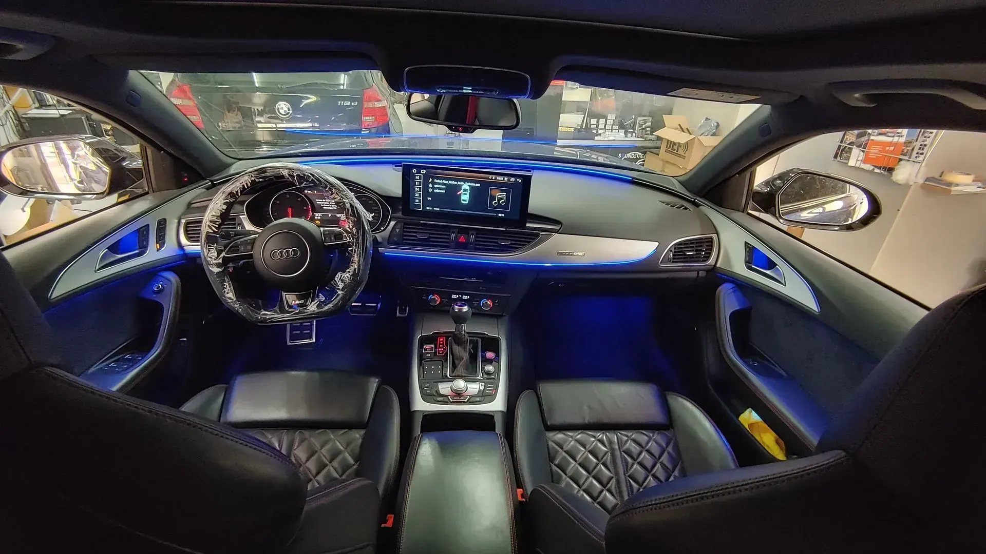 Vista interior de un automóvil Audi con iluminación ambiental azul, tablero negro y asientos de cuero acolchado.