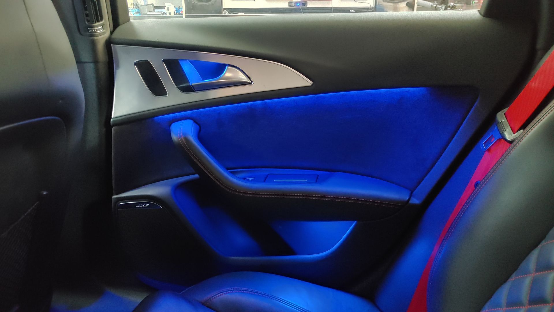 Interior de puerta de coche con iluminación ambiental azul y detalles en cuero negro.