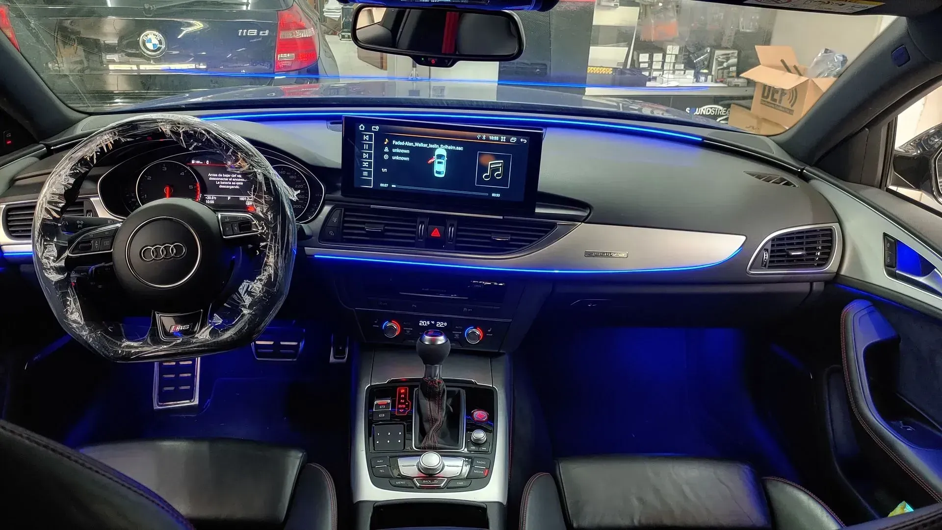 Interior del Audi con iluminación ambiental azul. Se ven el volante, el salpicadero con pantalla y la palanca de cambios.