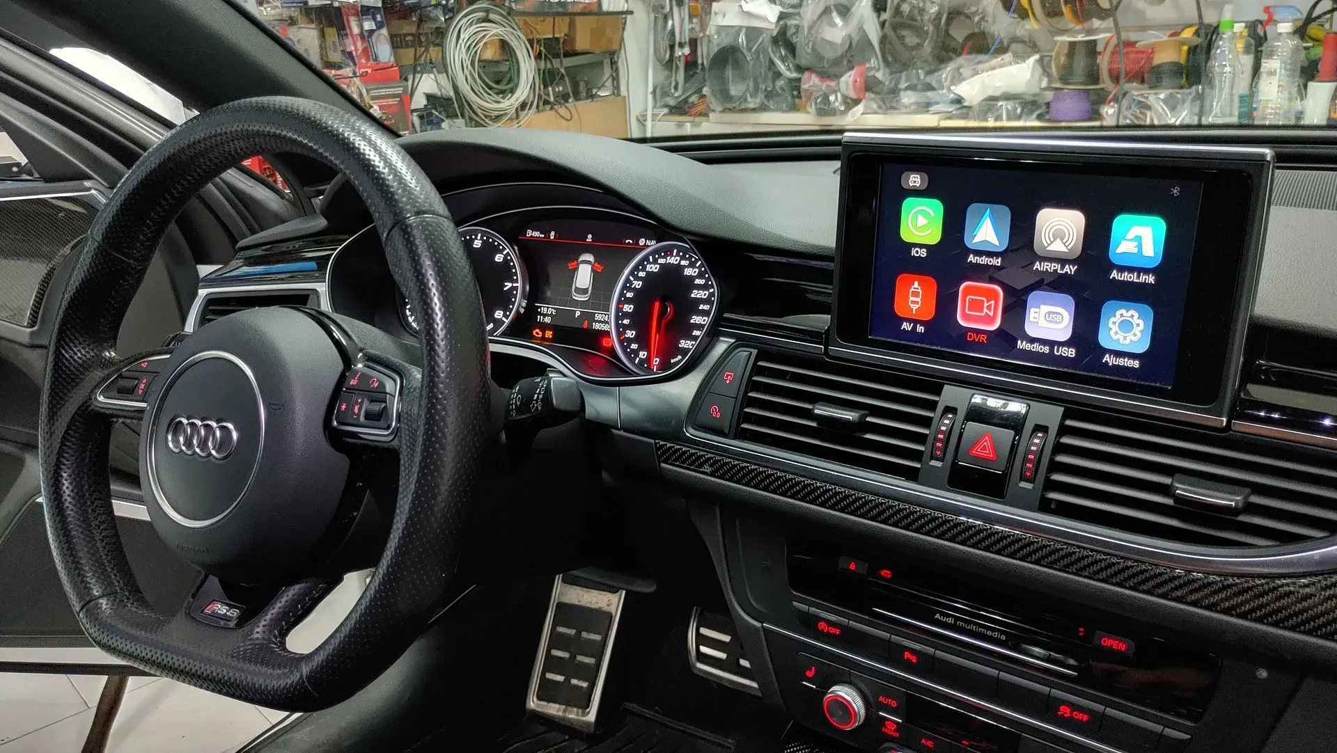 Interior de automóvil negro con volante, tablero digital y pantalla táctil que muestra íconos de aplicaciones.