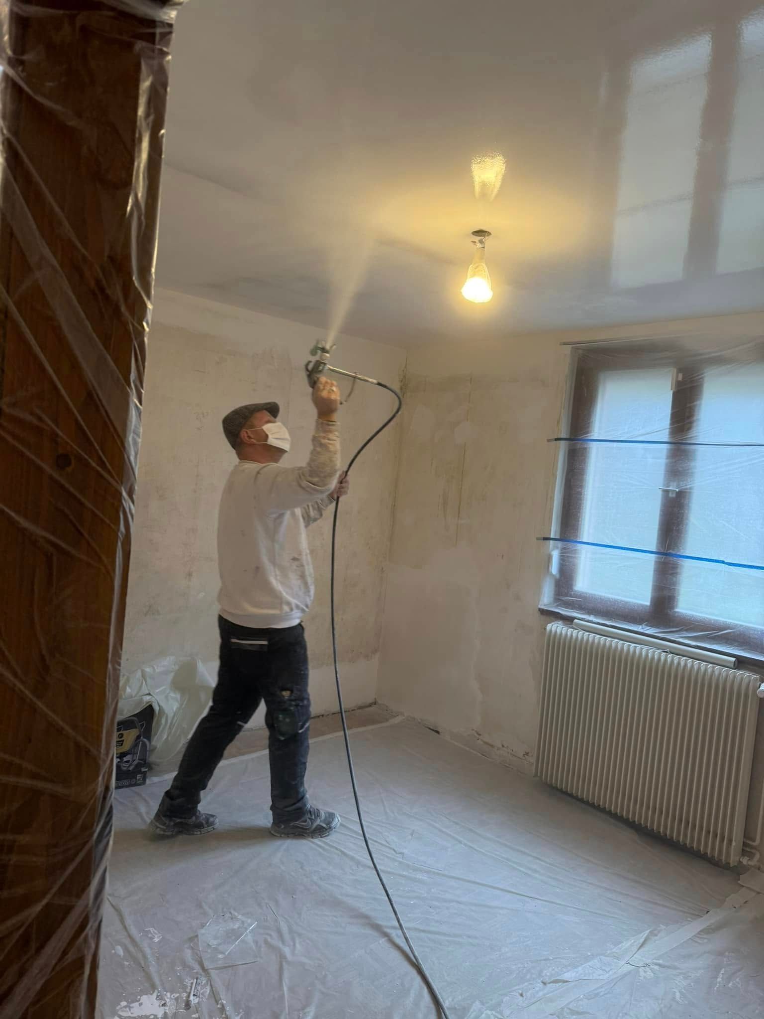 Un artisan projette de l'enduit au plafond.