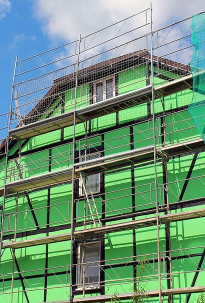 Des échafaudages entourent une maison en construction, à la façade vert vif et à la structure traditionnelle en bois noir.