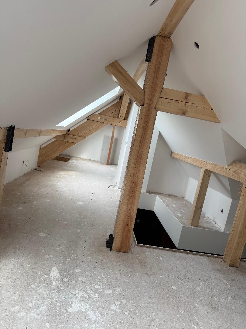 Une pièce mansardée inachevée avec des poutres de soutien en bois apparentes, des murs blancs inclinés