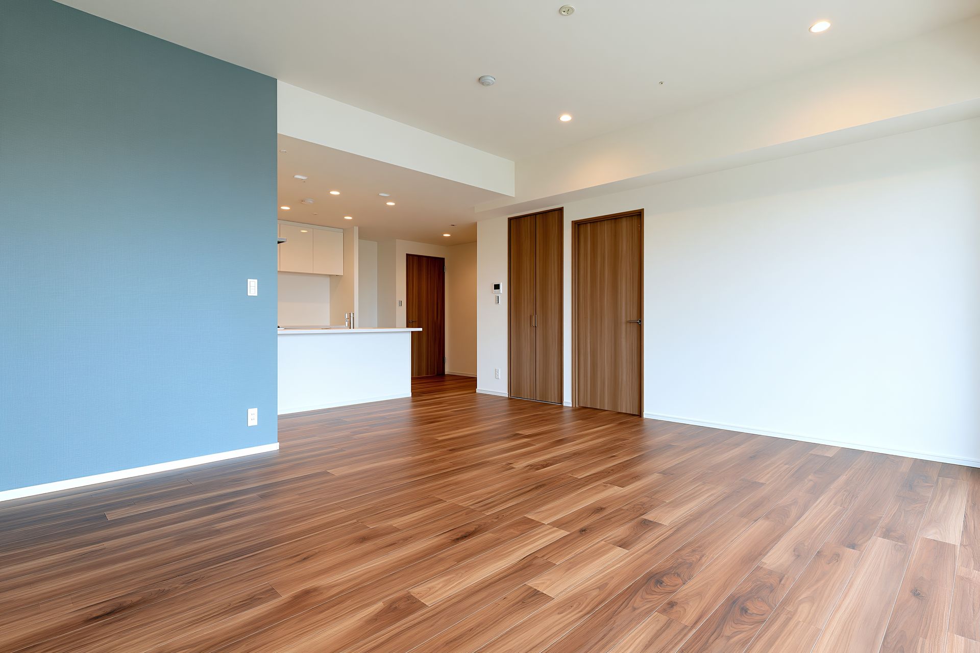 Salon moderne vide avec parquet, mur d'accent bleu, murs blancs et coin cuisine en arrière-plan