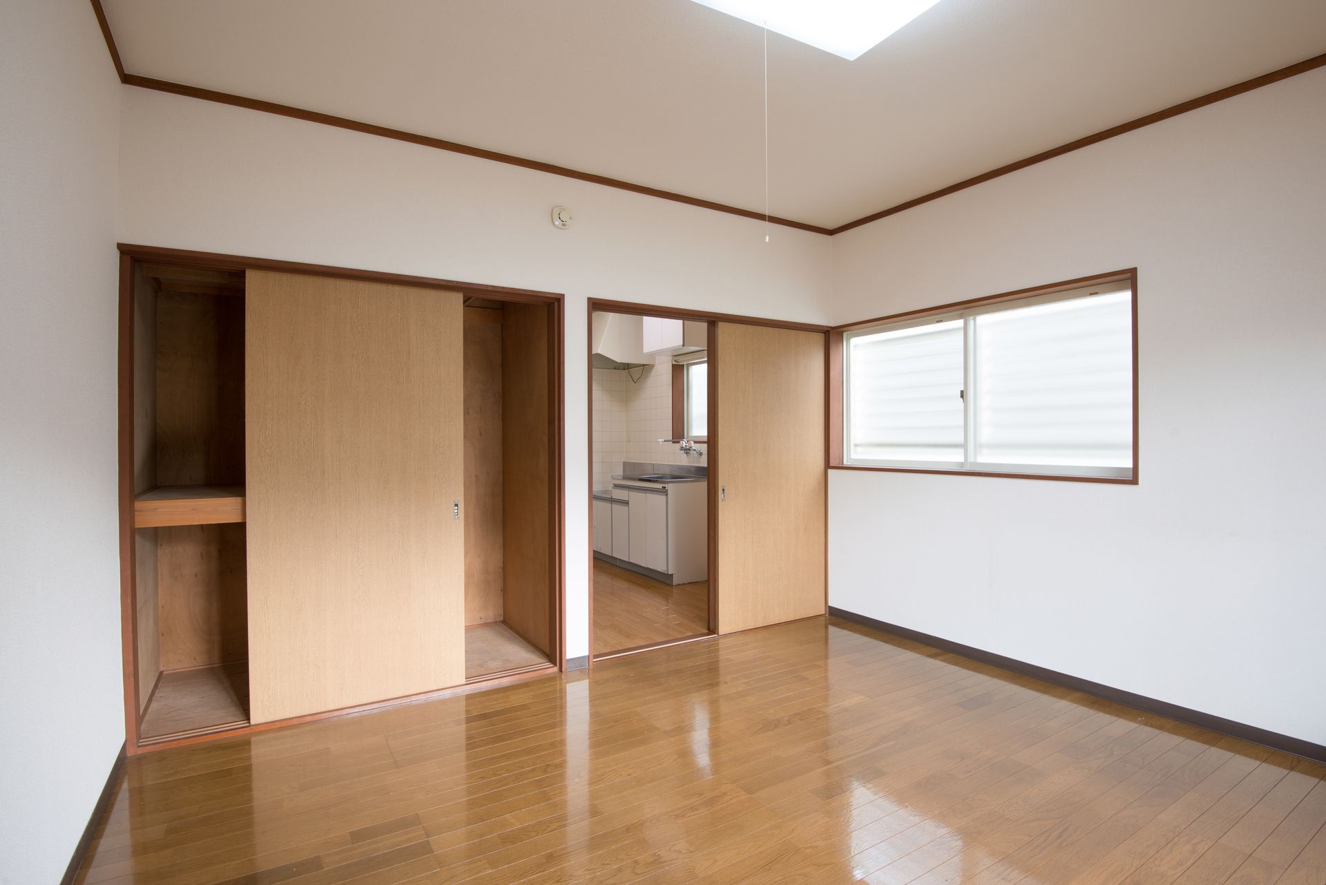 Pièce vide avec parquet, placard coulissant, porte ouverte et fenêtre laissant entrer la lumière du jour