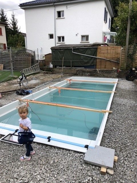 Ein kleines Kind steht neben einem im Bau befindlichen rechteckigen Pool; im Hintergrund ein weißes Haus.