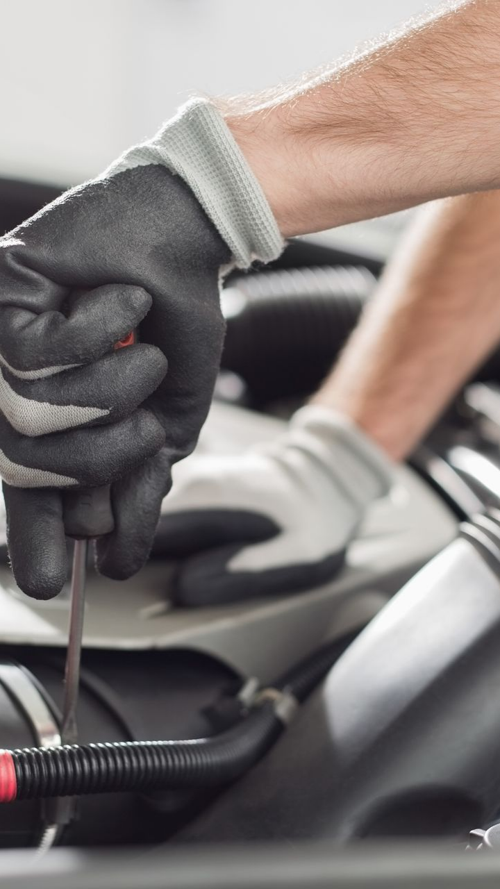 Les mains gantées d'un mécanicien utilisent un tournevis pour travailler sur un moteur de voiture.
