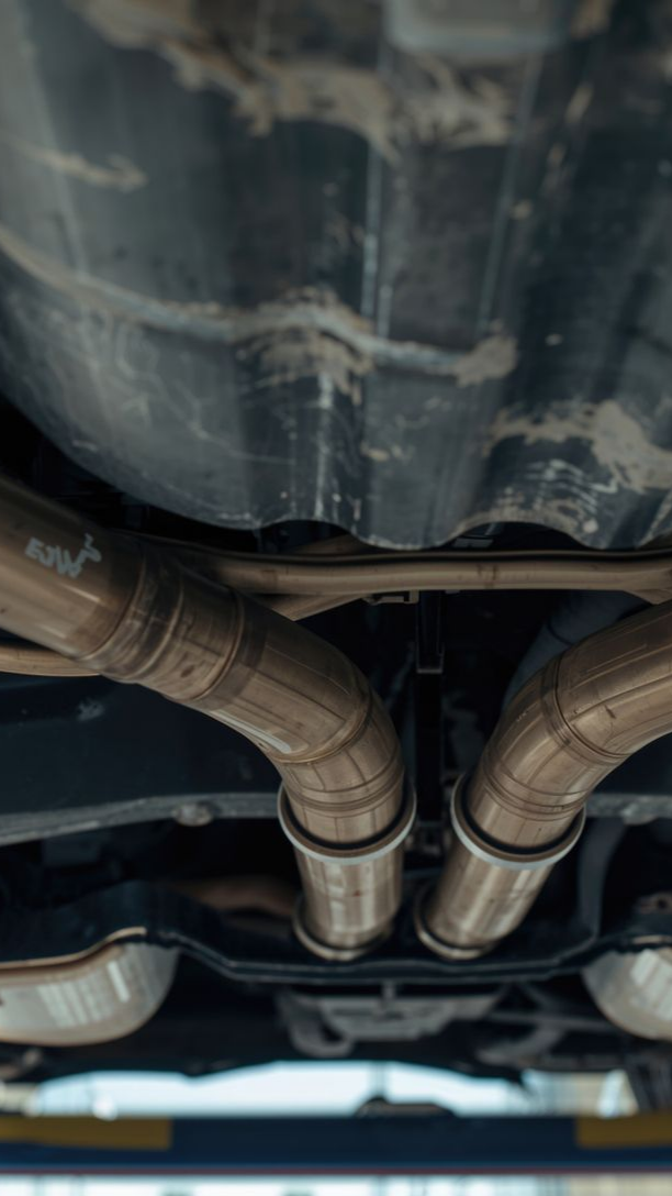 Dessous d'une voiture à double échappement dans un garage, montrant les tubes en acier inoxydable.