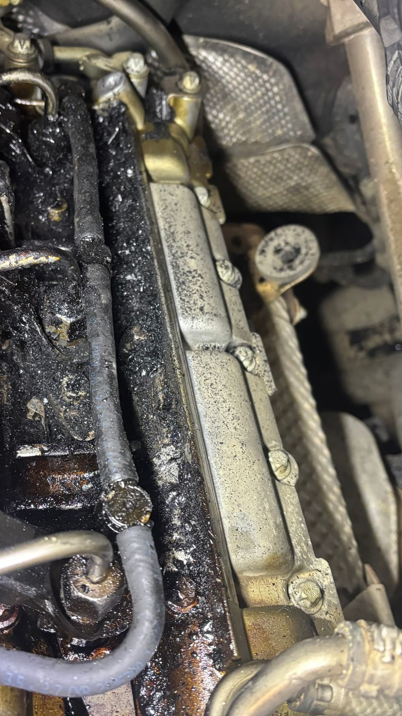 Compartiment moteur présentant une fuite d'huile noire sur des pièces métalliques, un câble et un écran thermique.