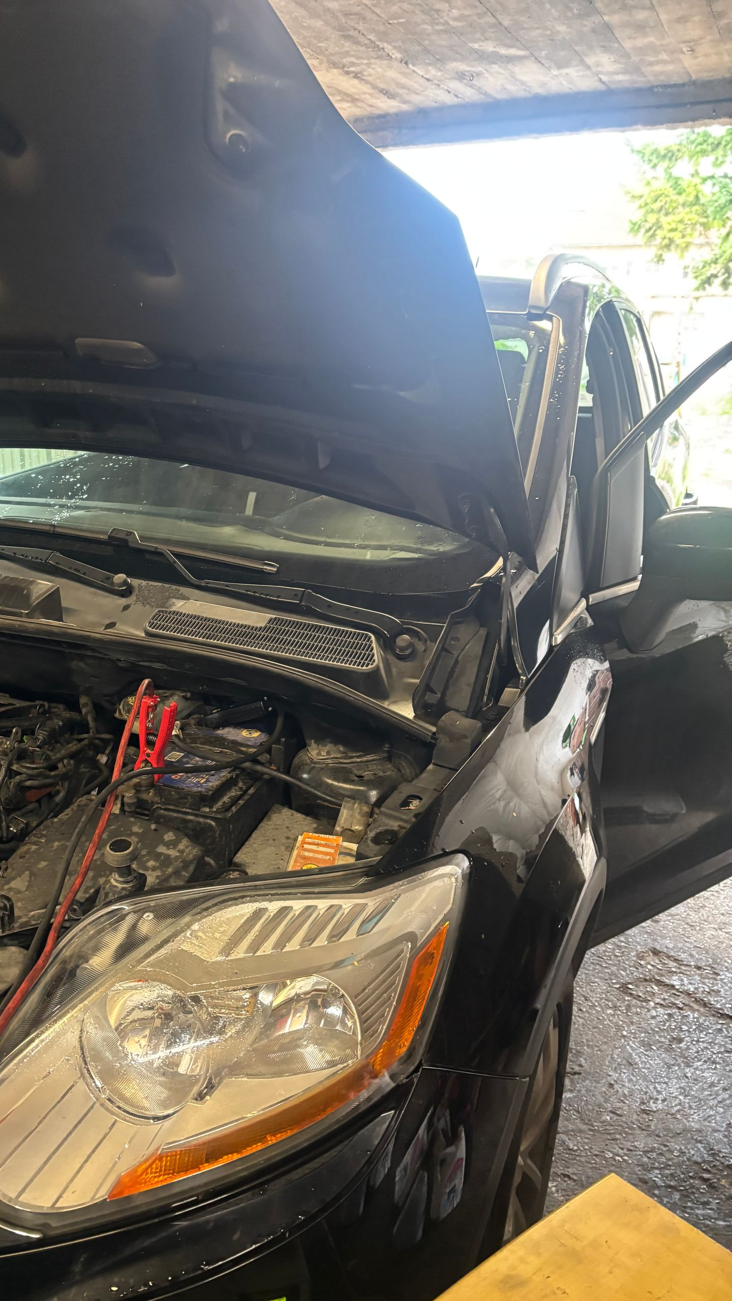 Voiture noire, capot ouvert, câbles de démarrage branchés au moteur.