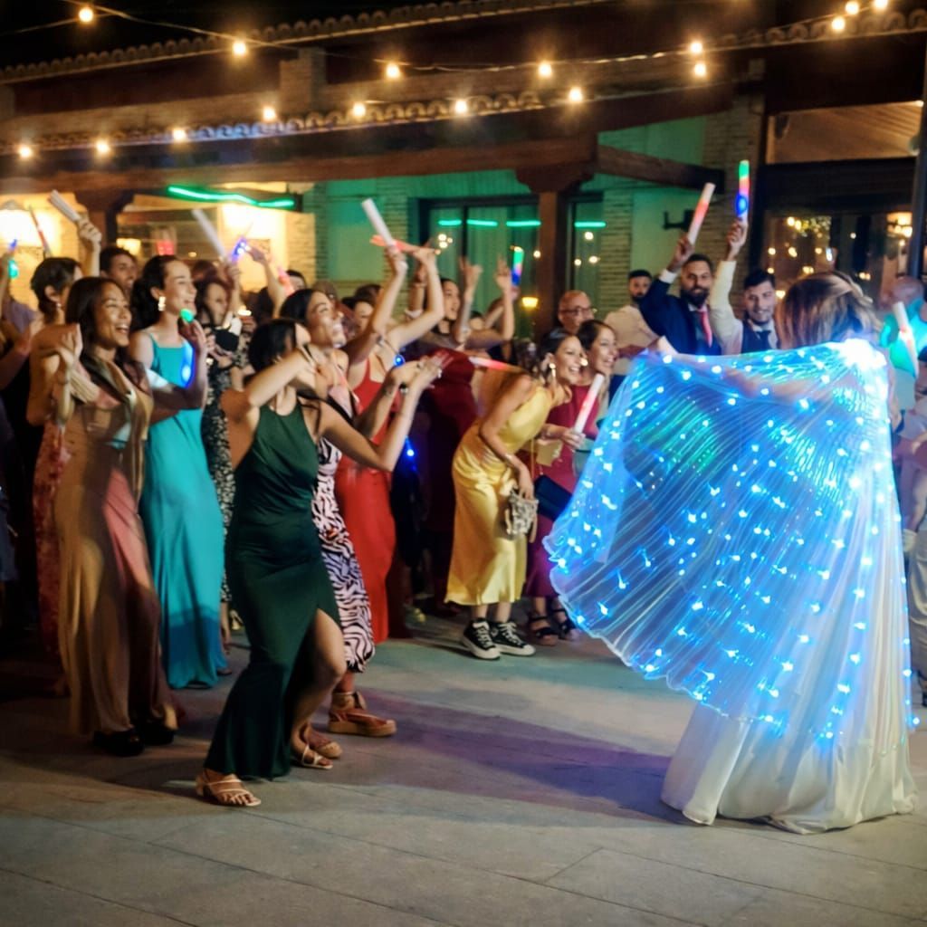 Recepción de boda: los invitados bailan al aire libre con palos luminosos y una novia que lleva una capa iluminada.