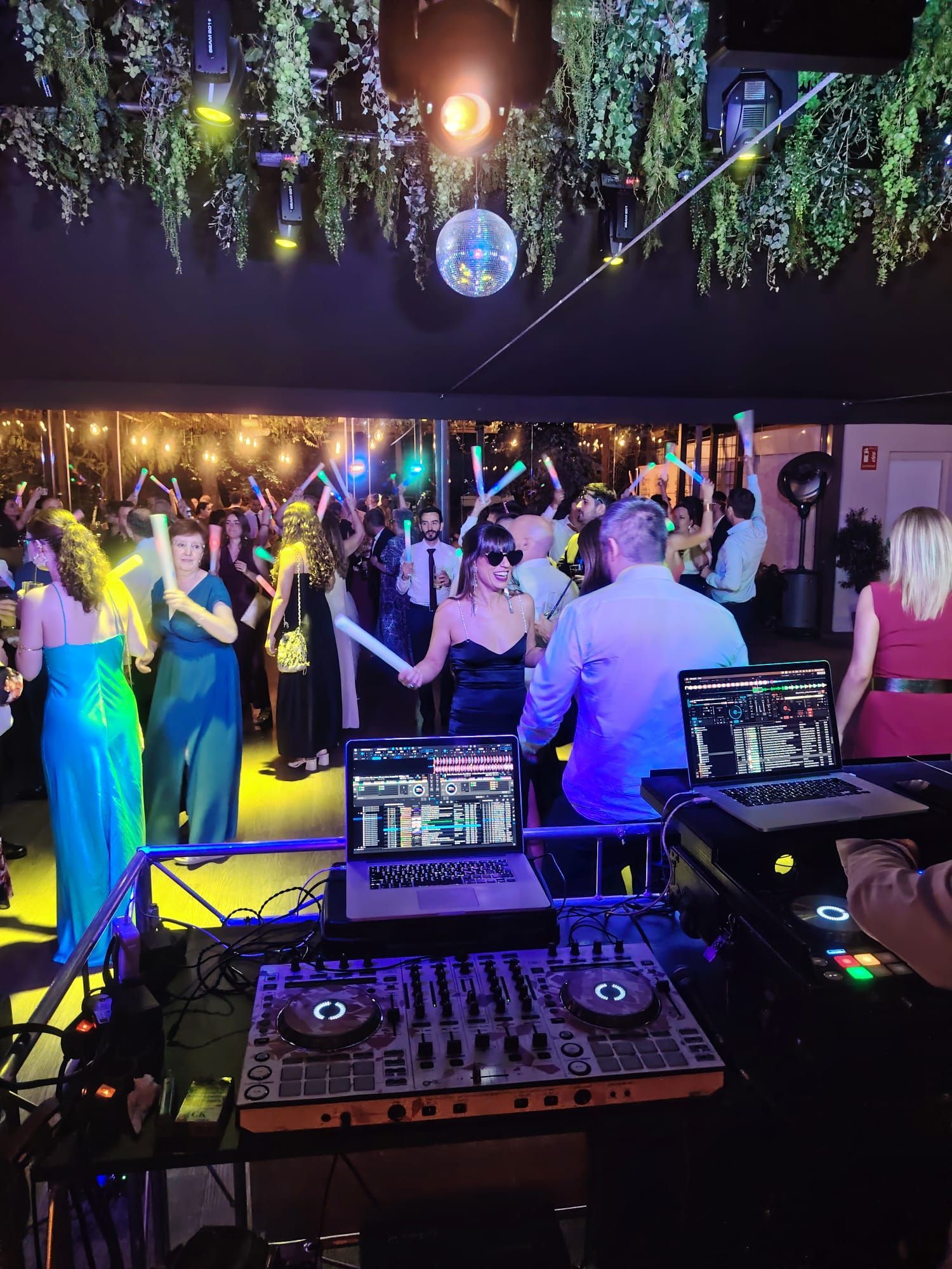 DJ en una fiesta con gente bailando; bola de discoteca, luces de colores.